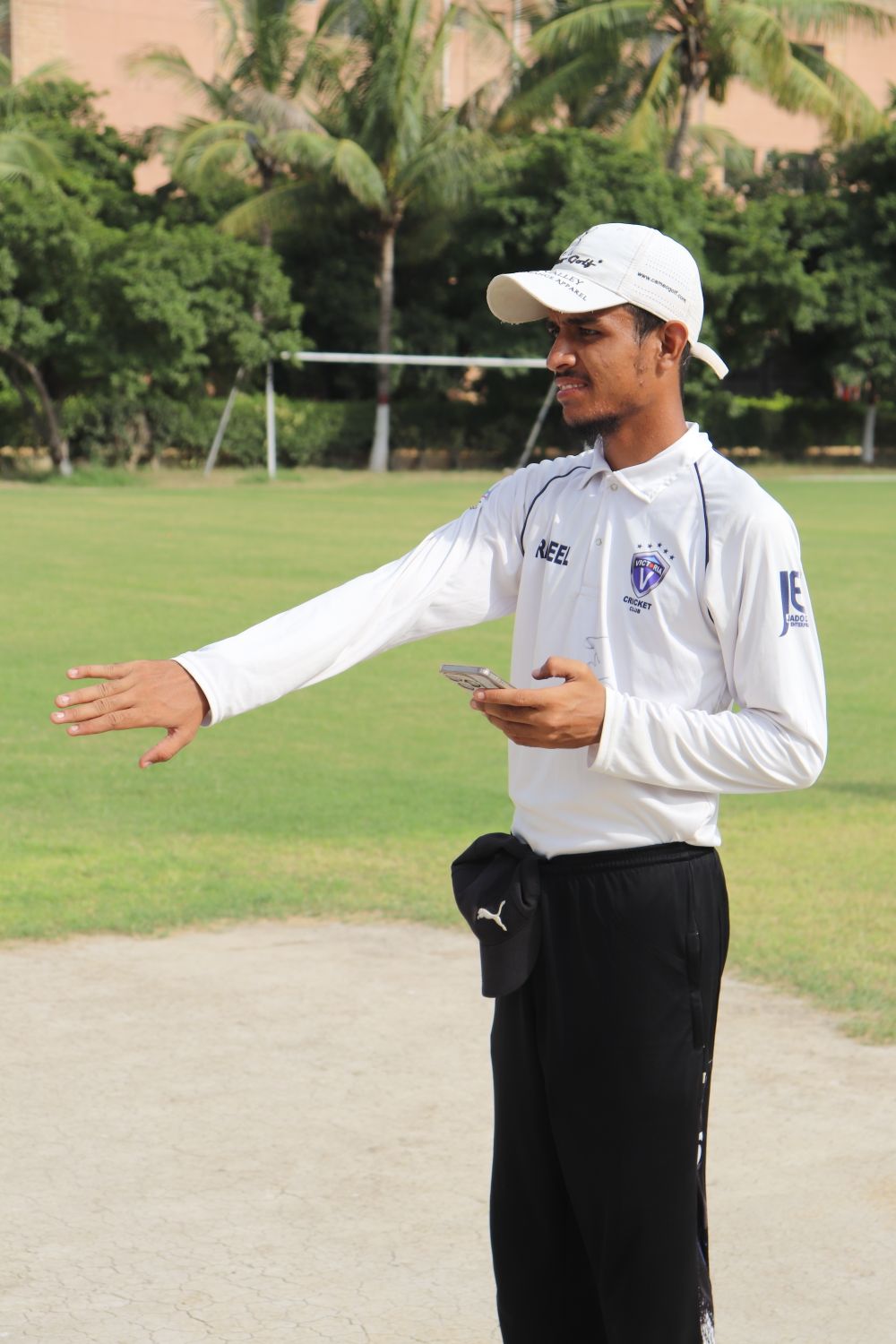 A cricket coach in white kit giving guidance beside a cricket ground in Karachi