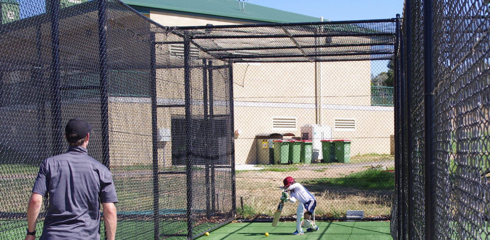 A coach watching a junior batter practise in outdoor cricket nets at Freebody Oval